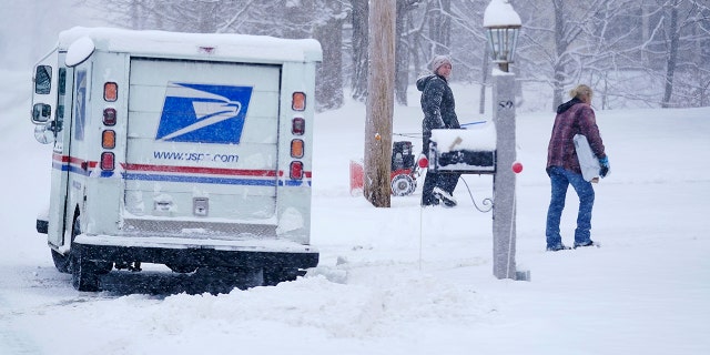 Un transportista del Servicio Postal de EE. UU. entrega un paquete durante una tormenta de nieve el viernes 7 de enero de 2022 en East Derry, New Hampshire.  Se espera que una tormenta de invierno deje caer alrededor de medio pie de nieve en el área.