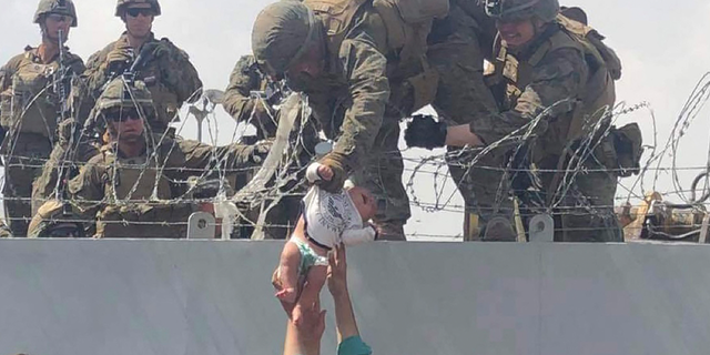 Американски морски пехотинец дърпа бебе през ограда от бодлива тел по време на евакуация на международното летище Хамид Карзай в Кабул, Афганистан, на 19 август 2021 г.