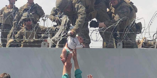 A U.S. Marine pulls an infant over a fence of barbed wire during an evacuation at Hamid Karzai International Airport in Kabul, Afghanistan, on August 19, 2021.