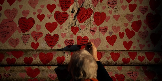 A woman writes a tribute message in a love heart of the National COVID Memorial Wall, in London, Wednesday, Jan. 12, 2022.