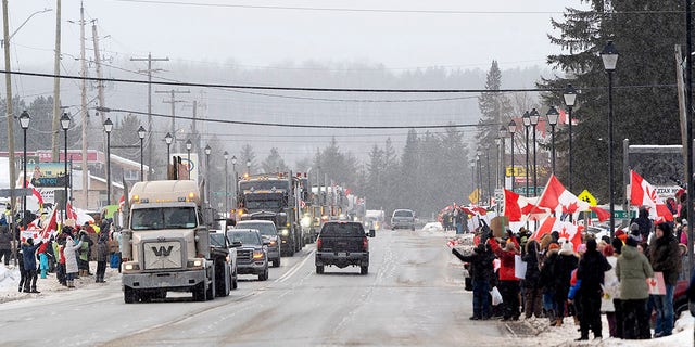 Protesters and supporters against a COVID-19 vaccine mandate for cross-border truckers cheer as a parade of trucks and vehicles pass through Kakabeka Falls outside of Thunder Bay, Ontario, op Woensdag, Jan.. 26, 2022. (David Jackson/The Canadian Press via AP)