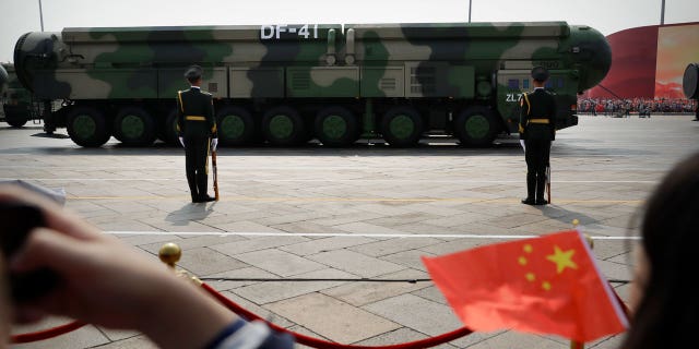 Spectators wave Chinese flags as military vehicles carrying DF-41 ballistic missiles roll during a parade to commemorate the 70th anniversary of the founding of Communist China in Beijing, Tuesday, Oct. 1, 2019.
