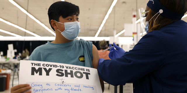 Un garçon de 13 ans tient une pancarte en faveur des vaccinations COVID-19 alors qu'il reçoit sa première vaccination Pfizer au département de santé publique du comté de Cook.