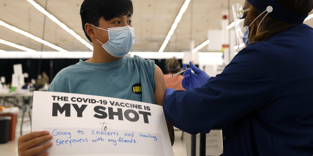 Lucas Kittikamron-Mora, 13, holds a sign in support of COVID-19 vaccinations as he receives his first Pfizer vaccination at the Cook County Public Health Department on May 13 in Des Plaines, Ill.