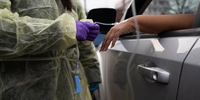 A health care worker attaches an IV infusion to a patient's hand during a monoclonal antibody treatment in the parking lot at Wayne Health Detroit Mack Health Center in Detroit, Michigan, Dec. 23, 2021.