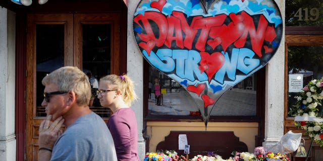In this Aug. 7, 2019 file photo, passersby walk past a makeshift memorial for the slain and injured victims of a mass shooting that occurred in the Oregon District in Dayton, Ohio. (AP Photo/John Minchillo, File)
