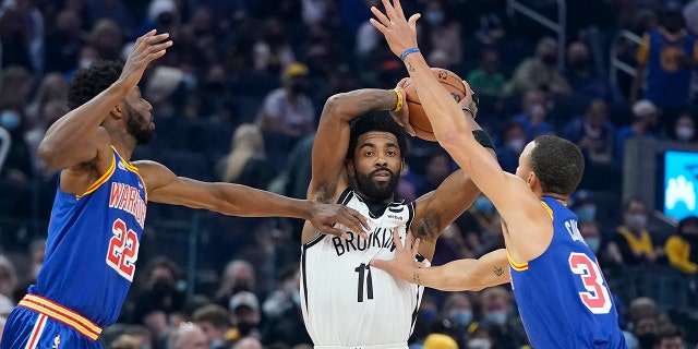 Brooklyn Nets guard Kyrie Irving (11) looks to pass the ball between Golden State Warriors forward Andrew Wiggins (22) and guard Stephen Curry during the first half of an NBA basketball game in San Francisco, Saturday, Jan. 29, 2022.