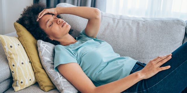 Sick young woman lying on the couch and holding her head with hand.