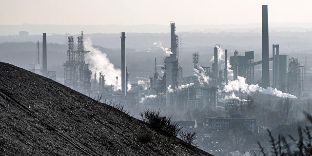 An oil refinery smokes behind a former coal dump in Gelsenkirchen, Germany on Monday, January 10, 2022.