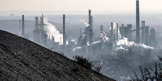 An oil refinery smokes behind a former coal mine dump in Gelsenkirchen, Germany, Monday, Jan. 10, 2022.