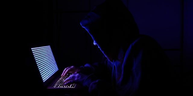 A person dressed as an internet hacker is seen with binary code displayed on a laptop screen in this illustration photo taken in Krakow, Poland, on Aug. 17, 2021.