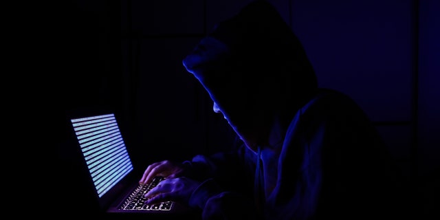 A person dressed as an internet hacker is seen with binary code displayed on a laptop screen in this illustration photo taken in Krakow, Poland, on Aug. 17, 2021.