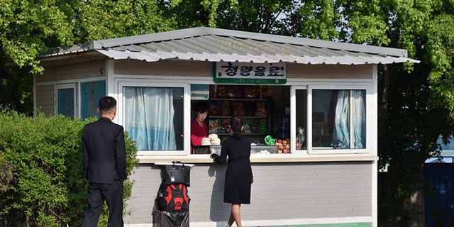 Pyongyang, Corea del Norte - 5 de mayo de 2019. Street View.  La mujer compra comida en una pequeña tienda en la calle.