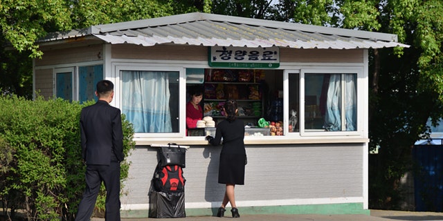 Pyongyang, Coreia do Norte - 5 de maio de 2019: Cena de rua.  Mulher compra mantimentos em uma pequena loja na rua.