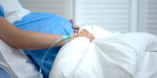 This file image shows a pregnant woman holding blanket at a hospital. 
