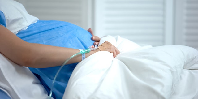 This file image shows a pregnant woman holding blanket at a hospital. 