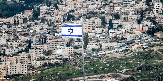 This photo taken on Jan. 24, 2020 from the Mount of Olives shows an Israeli flag fluttering (foreground) with the Abu Tor neighborhood in Jerusalem in the background. 