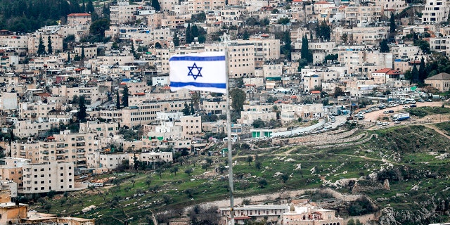 This photo taken on Jan. 24, 2020 from the Mount of Olives shows an Israeli flag fluttering (foreground) with the Abu Tor neighborhood in Jerusalem in the background.