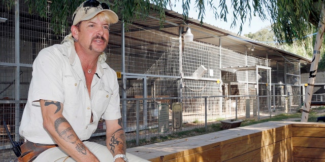 Joe Exotic sits in front of a big cat pen