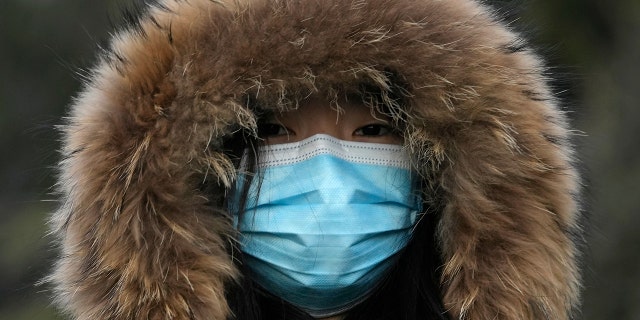 A woman wearing a mask to curb the spread of the coronavirus walks along a street in Beijing, China, Tuesday, Jan. 4, 2022