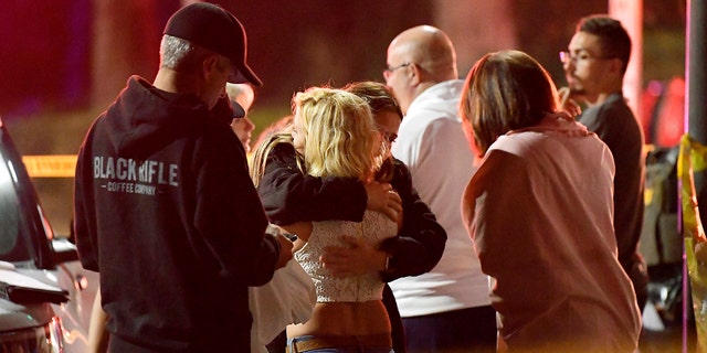 In this Nov. 8, 2018, file photo, people comfort each other as they stand near the scene of a shooting in Thousand Oaks, California, where a gunman opened fire inside a country dance bar crowded with hundreds of people. 