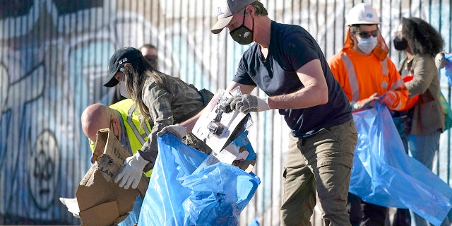 California Gov. Gavin Newsom, center, removes cardboard and other discarded items from a Union Pacific Railroad site on Thursday, Jan. 20, 2022, in Los Angeles.