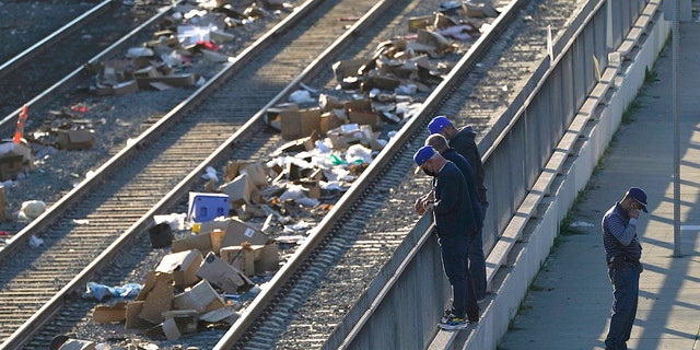 Homens observam uma pista na Union Pacific Railroad em Los Angeles na quinta-feira, 20 de janeiro de 2022.  O governador Gavin Newsom prometeu coordenação estadual na perseguição aos ladrões, que carregam contêineres de carga em trens perto da cidade de Los Angeles há meses, deixando os trilhos cobertos com caixas descartadas. 