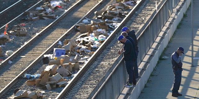 Homens observam uma pista na Union Pacific Railroad em Los Angeles na quinta-feira, 20 de janeiro de 2022.  O governador Gavin Newsom prometeu coordenação estadual na perseguição aos ladrões, que carregam contêineres de carga em trens perto da cidade de Los Angeles há meses, deixando os trilhos cobertos com caixas descartadas. 