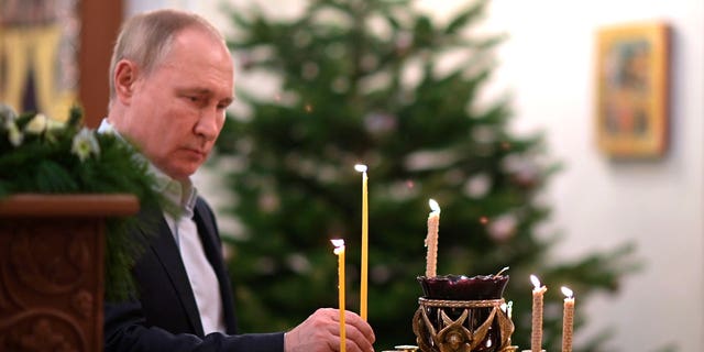 Russian President Vladimir Putin lights a candle during the Orthodox Christmas Liturgy in Novo-Ogaryovo, outside Moscow, Russia, late Thursday, Jan. 6, 2022. (Alexei Nikolsky/Sputnik, Kremlin Pool Photo via AP)