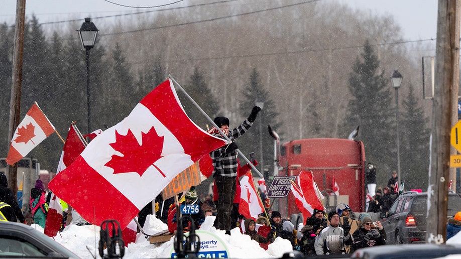 Protesters and supporters against a COVID-19 vaccine mandate for cross-border truckers cheer as a parade of trucks and vehicles pass through Kakabeka Falls outside of Thunder Bay, Ontario, on Wednesday, Jan. 26, 2022. (David Jackson/The Canadian Press via AP)