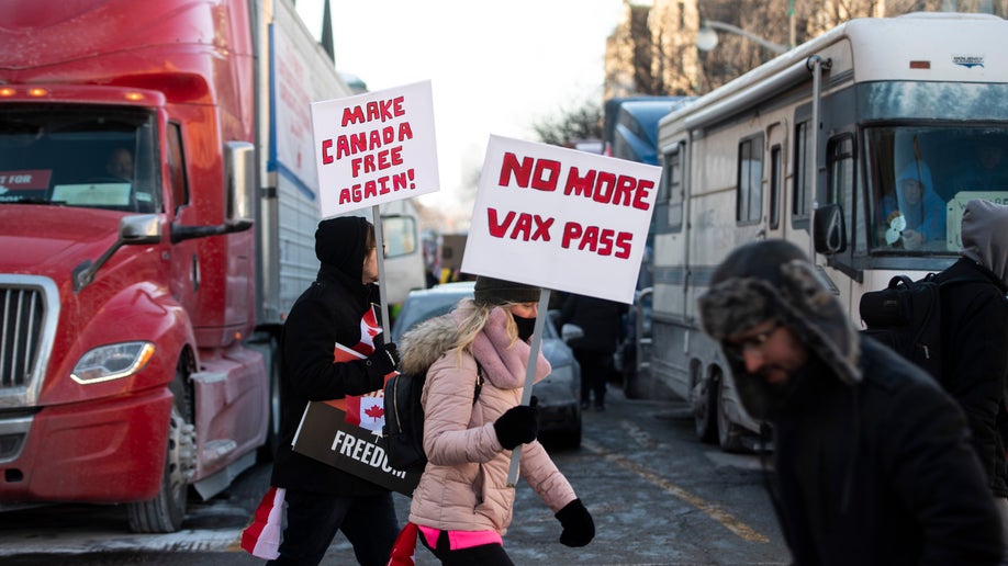People walk in front of trucks parked on Wellington Street as they join a rally against COVID-19 restrictions on Parliament Hill, which began as a cross-country convoy protesting a federal vaccine mandate for truckers, in Ottawa, on Saturday, Jan. 29, 2022. (Justin Tang/The Canadian Press via AP)