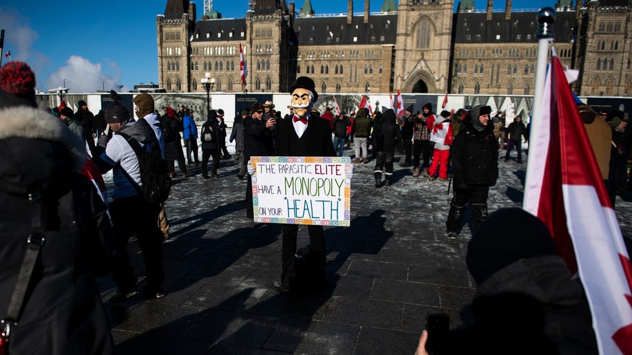 A person wearing a Monopoly Man mask holds a sign during a rally against COVID-19 restrictions on Parliament Hill, which began as a cross-country convoy protesting a federal vaccine mandate for truckers, in Ottawa
