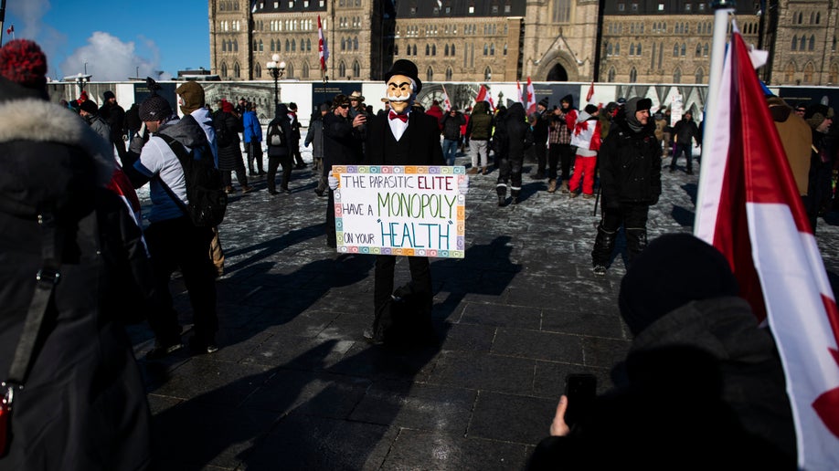 A person wearing a Monopoly Man mask holds a sign during a rally against COVID-19 restrictions on Parliament Hill, which began as a cross-country convoy protesting a federal vaccine mandate for truckers, in Ottawa