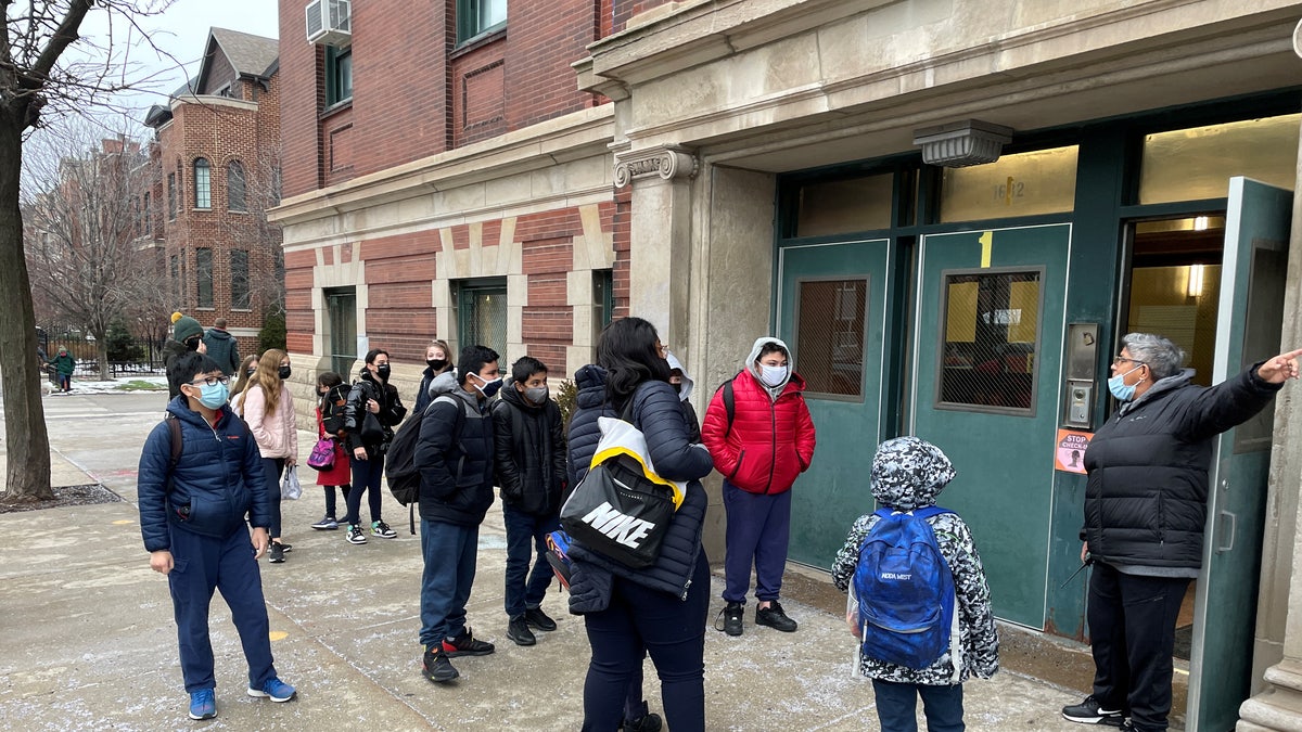Students wearing face masks line up outside the entrance of Prescott Elementary School while directed by school staff in Chicago, Illinois, U.S. January 12, 2022. 