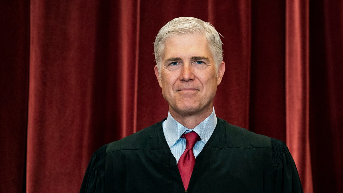 Justice Neil Gorsuch in robes against red curtain