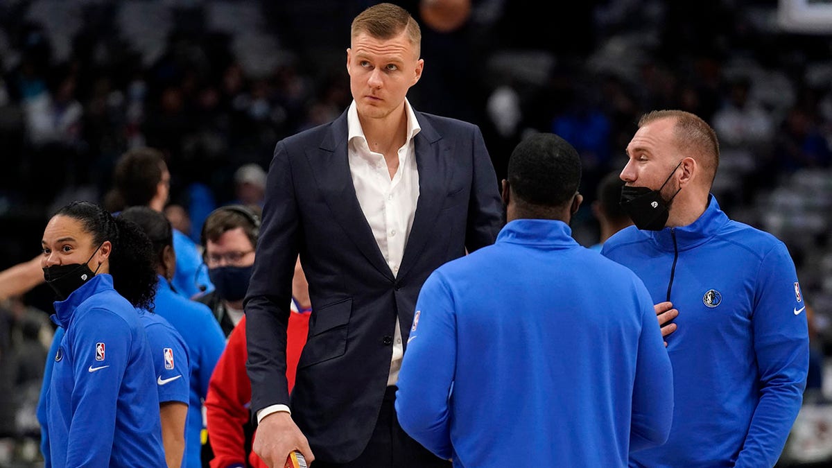 Dallas Mavericks' Kristaps Porzingis, center, stands on the court talking with staff before the first half of a NBA basketball game against the Oklahoma City Thunder in Dallas, Wednesday, Feb. 2, 2022. Porzingis did not play in the game.