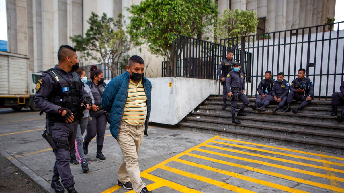 David Coronado Perez, who is allegedly part of a human trafficking network, is escorted by an officer at the end of his court hearing, in Guatemala City, Friday, Feb. 4, 2022. (AP Photo/Oliver de Ros)