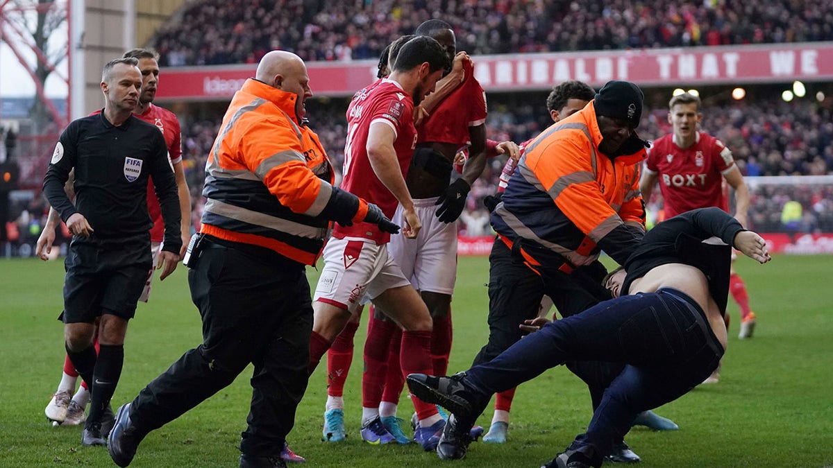 Stewards block a man who invaded the pitch as Nottingham Forest celebrate scoring their side's third goal, during the English FA Cup fourth round soccer match between Nottingham Forest and Leicester City at the City Ground, Nottingham, England, Sunday, Feb. 6, 2022. Police have arrested a man who appeared to attack Nottingham Forest players as they celebrated one of their goals in an FA Cup victory over Leicester. A supporter emerged from the away section of the City Ground before striking out at Forest players as they celebrated the third in a 4-1 win over the cup holders.