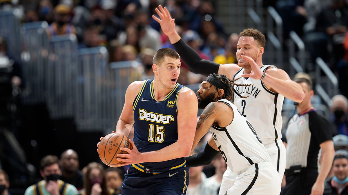 Denver Nuggets center Nikola Jokic, left, looks to pass the ball as Brooklyn Nets guard DeAndre' Bembry, center, and forward Blake Griffin defend in the first half of an NBA basketball game Sunday, Feb. 6, 2022, in Denver.