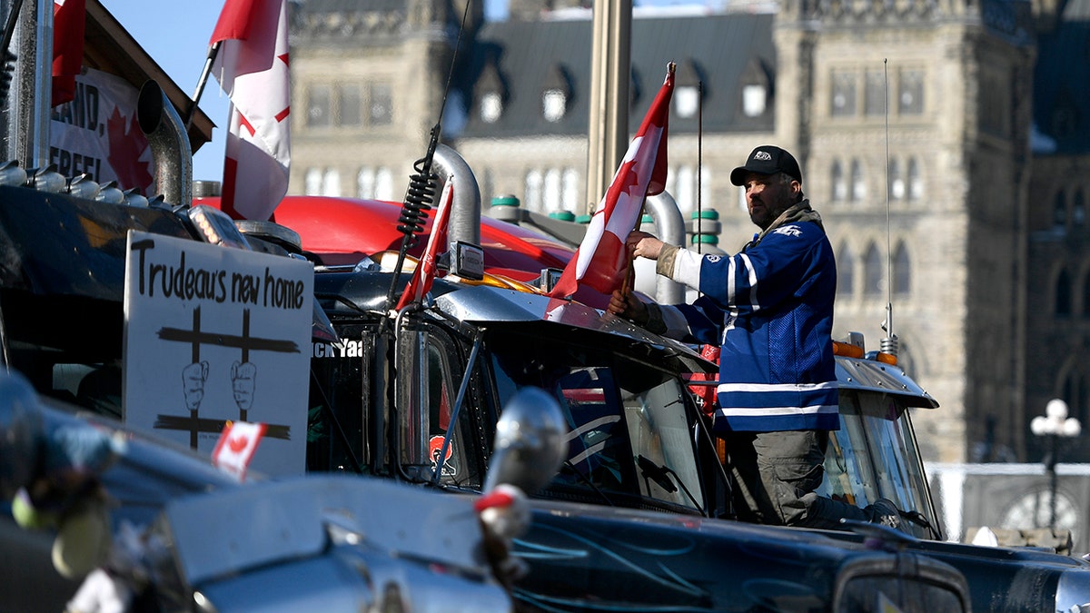 A protester affixes a flag to the top of a truck, parked beside another with a sign calling for the jailing of Prime Minister Justin Trudeau, outside Parliament Hill, as a protest against COVID-19 restrictions continues into its second week in Ottawa on Monday, Feb. 7, 2022. (Justin Tang/The Canadian Press via AP)