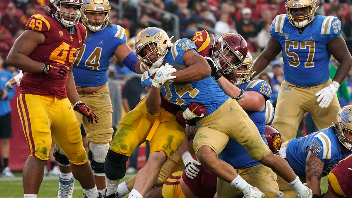 FILE - UCLA running back Zach Charbonnet (24) runs the ball in for a touch down as Southern California defensive lineman Jacob Lichtenstein (97) tries to stop him during the second half of an NCAA college football game Saturday, Nov. 20, 2021, in Los Angeles. An advocacy group for college athletes has filed a complaint with the National Labor Relations board in the next step in a push to give employee status to college athletes and afford them the right to competitive pay, collective bargaining and other benefits and protections. The National College Players Association on Tuesday, Feb. 8, 2022 filed the unfair labor practice charges against the NCAA, Pac-12 Conference, UCLA and the University of Southern California.