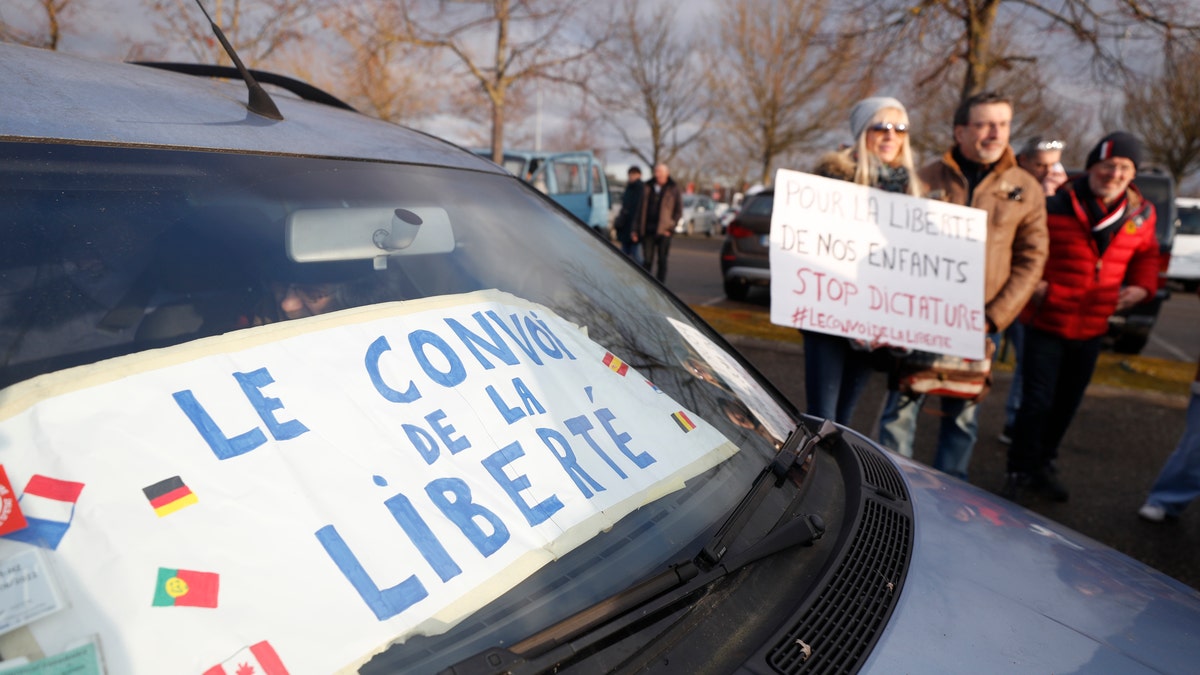 Protesters hold a placard next to car part of the "Freedom Convoy" and heading to Paris, Friday, Feb.11, 2022 in Strasbourg, eastern France. 