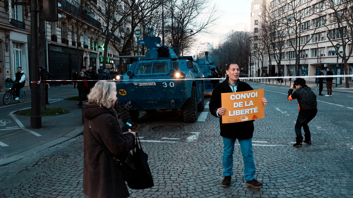 A protestor holding a placard reading "Freedom convoy" poses in front of a armoured vehicle during a protest, in Paris, Friday, Feb. 11, 2022.