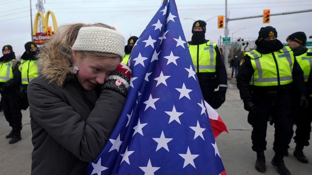 A supporter holding an American flag cries as police officers enforce an injunction against their demonstration, which has blocked traffic across the Ambassador Bridge by protesters against COVID-19 restrictions, in Windsor, Ont., Saturday, Feb. 12, 2022. THE CANADIAN PRESS/Nathan Denette