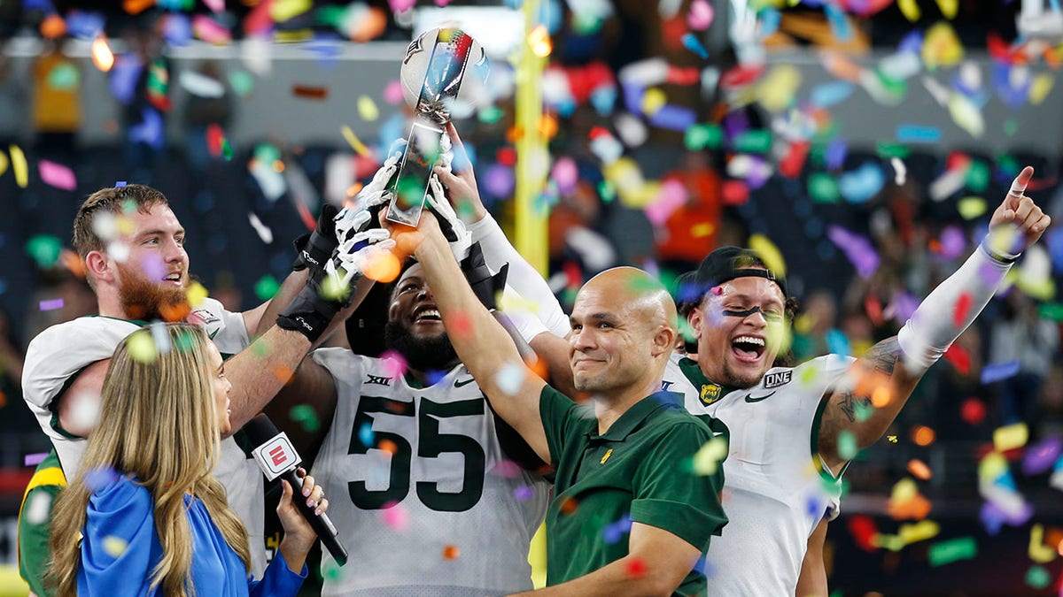 FILE - Baylor offensive linemen Connor Galvin, left, and Xavier Newman-Johnson (55), head coach Dave Aranda, and linebacker Terrel Bernard, right, hold up the trophy as ABC commentator Molly McGrath looks on after an NCAA college football game against Oklahoma State for the Big 12 Conference championship in Arlington, Texas, Saturday, Dec. 4, 2021. Aranda has agreed to a contract extension through the 2028 season after leading the Bears to a Big 12 championship and a school-record 12 wins capped by a Sugar Bowl victory last season. The school announced the extension Tuesday, Feb. 15, 2022, two months after athletic director Mack Rhoades had said there was a verbal agreement in amend the coach's contract.
