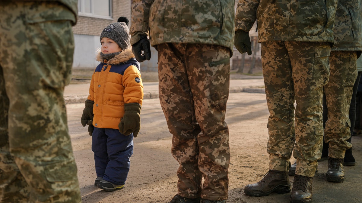 A child copies the position of Ukrainian servicemen standing at attention during the national anthem during an event marking a Day of Unity in Sievierodonetsk, the Luhansk region, eastern Ukraine, Wednesday, Feb. 16, 2022. 