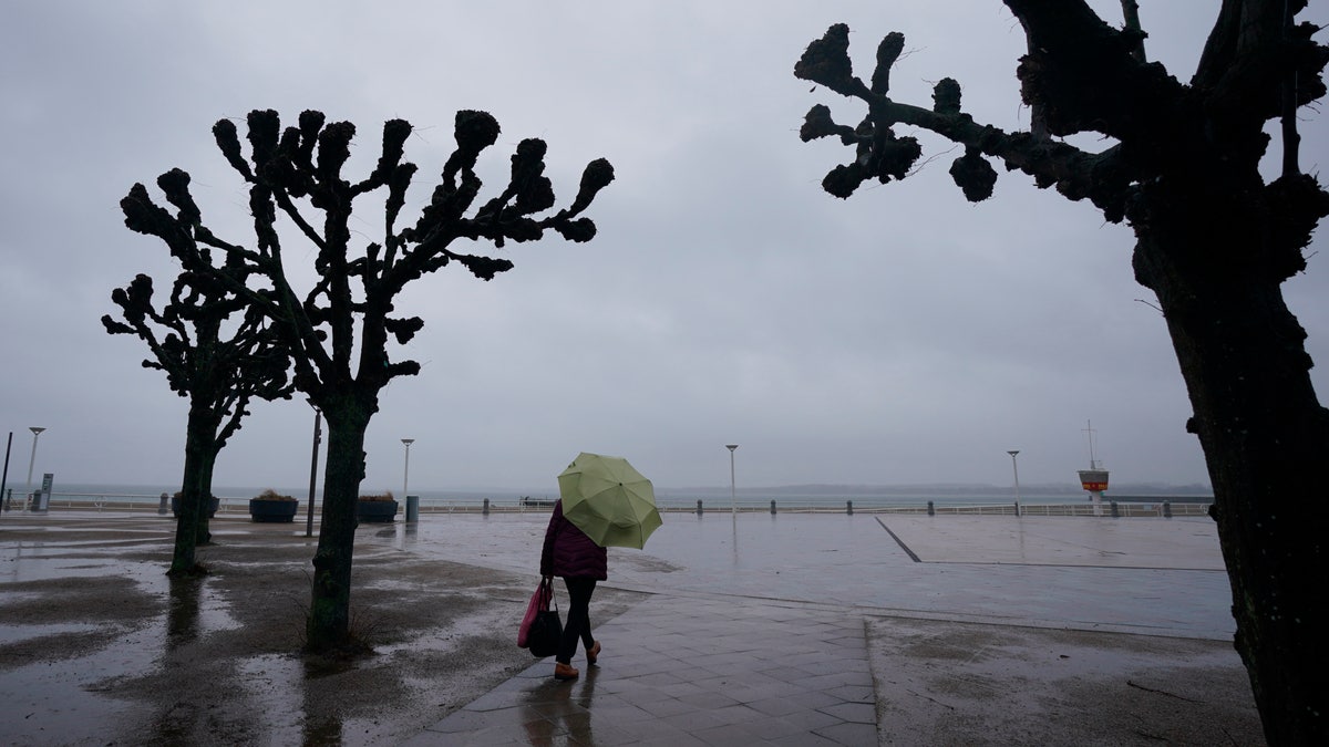A passerby walks in the rain along the deserted promenade at the Baltic Sea in Travemuende, Germany, Friday, Feb. 18, 2022.