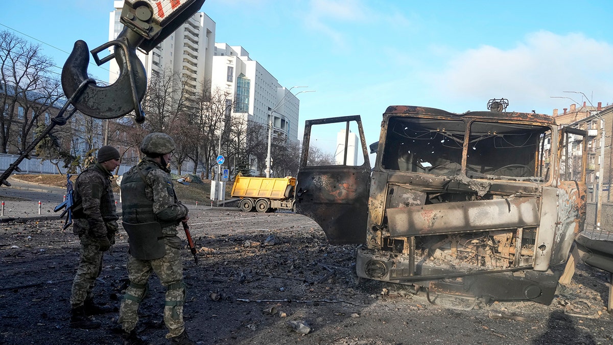 Ukrainian soldiers stand next to a burnt military truck, in a street in Kyiv, Ukraine, Saturday, Feb. 26, 2022. Russian troops stormed toward Ukraine's capital Saturday, and street fighting broke out as city officials urged residents to take shelter.