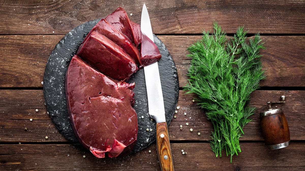 Raw liver on slate board on wooden background top view