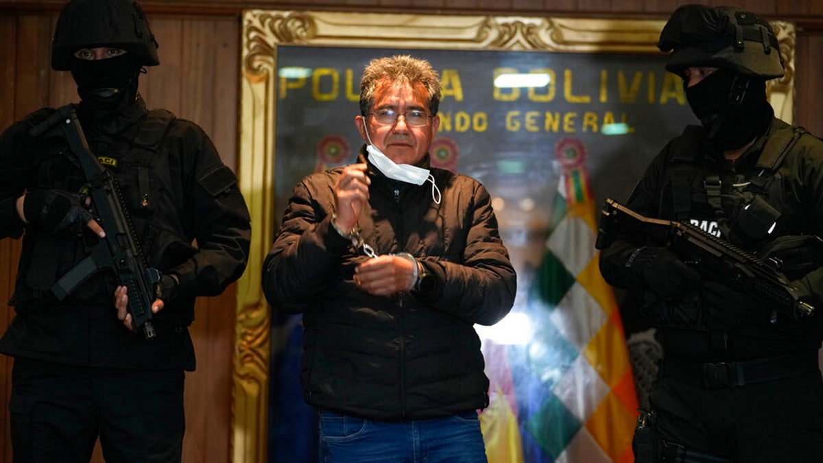 FILE: Police escort former police colonel Maximiliano Davila as he was presented to the media at a Bolivian Police Command office, in La Paz, Bolivia, Sunday, Jan. 23, 2022.